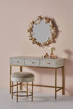 a dressing table with a mirror and stool in front of it, against a pink wall