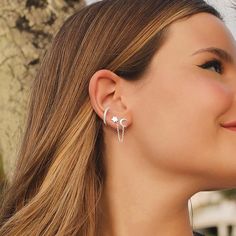 a woman wearing earrings with the moon and star design on her ear, standing next to a tree