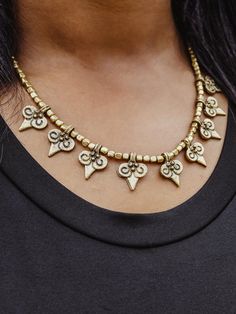 This stunning necklace features gold fleur de lis beads — a beautiful way to keep this emblem of luck, light and life near you at all times! Dress up a casual outfit or wear it on a night out — this eye-catching handmade necklace is a one-of-a-kind creation handcrafted by local artisans in Langtang, Nepal. Gold Necklaces With Heart-shaped Round Beads, Gold Necklaces With Round Heart Beads, Gold Necklace With Heart And Round Beads, Gold Heart Beaded Choker Jewelry, Gold Heart Beads Choker Jewelry, Gold Heart Beads Choker Necklace, Spiritual Festival Jewelry With Dangling Beads, Gold Necklaces With Metal Beads, Festival Brass Beaded Necklace