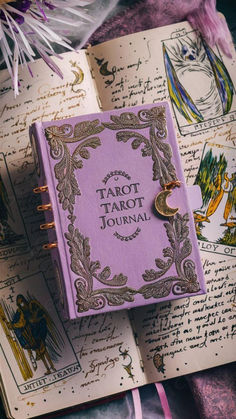 a purple book sitting on top of an open book next to some flowers and feathers