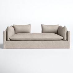 a beige couch sitting on top of a white floor next to a wall with two pillows