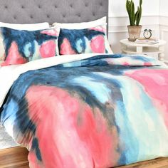 a bed with colorful comforter and pillows on it in a room next to a potted plant