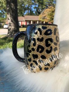 a black and gold leopard print coffee mug sitting on top of a white fluffy blanket