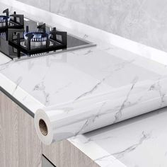 a kitchen counter with white marble and black burners on it's side, next to a roll of toilet paper