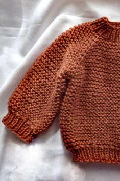 an orange knitted sweater laying on top of a white sheet