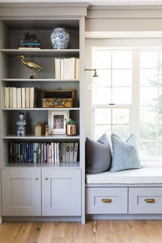 a window seat in the corner of a room with bookshelves and pillows on it