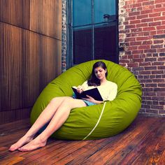 a woman sitting on an orange bean bag chair reading a book