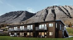 a brown house sitting in the middle of a lush green field with mountains behind it