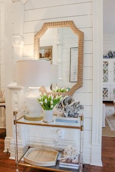 a table with a mirror, vase and flowers on it in front of a white wall