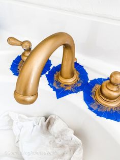 two golden faucets sitting on top of a white sink next to blue towels