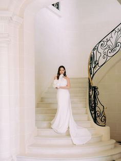 a woman in a white dress standing on some stairs with her arms crossed and looking at the camera