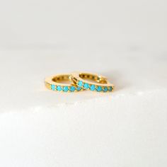 "Elegant and dainty, these tiny huggie hoops are prong-set with vibrant turquoise gemstones all around the hoop and are a beautiful addition to your everyday lineup. Subtle, versatile and perfect to mix and match with other earrings. * D E T A I L S * ∙ Sold individually (1 earring) or as a pair (2 earrings) ∙ Material: .925 Sterling Silver or 18K Gold Plated over .925 Sterling Silver ∙ Turquoise stones ∙ Outer Diameter: 10mm / Inner Diameter: 6.5mm ∙ Hypoallergenic & nickel-free * P A C K A Ear Huggies, Turquoise Earrings Gold, Gold Huggie Earrings, Ear Jacket Earring, Cartilage Hoop, 2 Earrings, Tiny Earrings, Turquoise Stones, Huggie Earrings