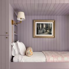 a bedroom with purple walls and white bedspread, framed artwork on the wall