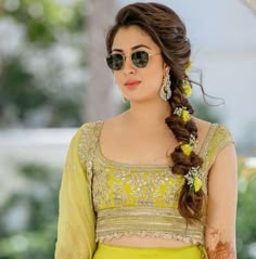 a woman in a yellow sari and sunglasses with her hair pulled into a braid