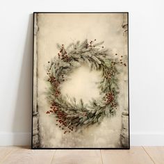 a framed photograph of a christmas wreath with berries and pine cones on it, against a white wall