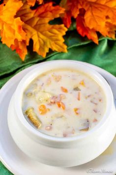 a white bowl filled with soup on top of a plate next to fall colored leaves