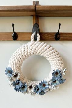 a white rope wreath with blue flowers hangs on a hook in front of a wall