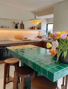 a green tiled table with stools and flowers in a vase on the counter top