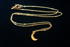 A rich golden moon has been set on dainty twinkling gold chains to create this gorgeous enchanting necklace, perfectly suited for layering. The 7x12mm 24k gold plated moon charm rests on 1.7mm 24k gold plated chains interspersed with tiny twinkling gold bars. This necklace is finished with a 24k gold plated lobster claw clasp. This necklace is shown paired with a matching starlit gold choker necklace. You can find that necklace sold separately here: https://www.etsy.com/listing/664002306/starlit Gold Celestial Necklace For Party, Gold Jewelry With Moon Charm For Party, Gold Necklace With Moon Charm For Party, Gold Crescent Charm Necklace With Delicate Chain, Gold Moon Charm Necklace For Parties, Gold Dainty Moon Charm Necklace, Gold Moon Charm Necklace With Delicate Chain, Dainty Gold Moon Charm Necklace, Elegant Layered Necklace With Moon Charm As Gift