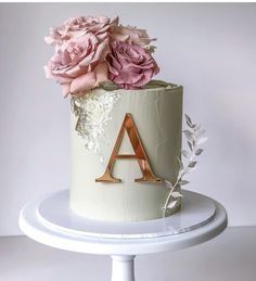 a white cake with pink flowers and the letter a on top is sitting on a pedestal