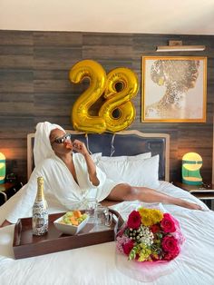 a woman sitting on top of a bed next to a tray with food and drinks