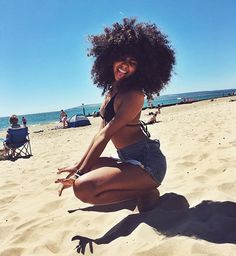 a woman sitting on top of a sandy beach next to the ocean with her feet in the air