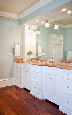 a bathroom with double sinks and two mirrors on the wall next to white cabinetry