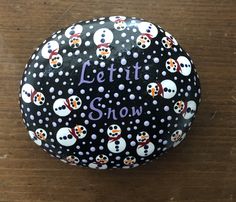 a black and white painted rock with snowmen on it that says let it snow