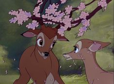 two deer standing next to each other under a tree with pink flowers on its head