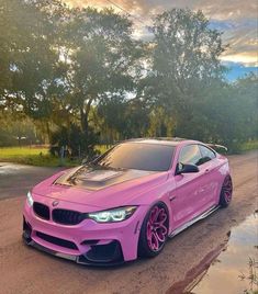 a pink car parked on the side of a road next to some grass and trees