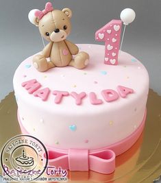 a pink birthday cake with a teddy bear on top and the number one candle in the middle