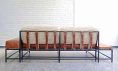 three woven baskets sitting on top of a metal frame with brown leather seats in front of a white brick wall