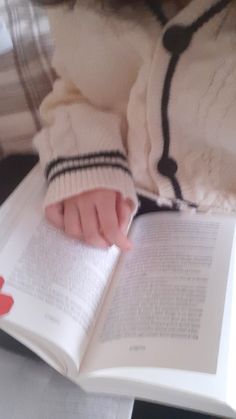 a person laying down reading a book with their hand on top of the open book