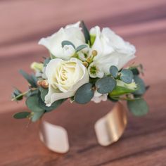 a bouquet of white flowers and greenery in a gold ring on a wooden table