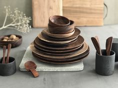 a stack of wooden bowls and spoons sitting on top of a table next to cups