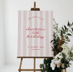 a pink and white striped birthday card on an easel with flowers in the foreground