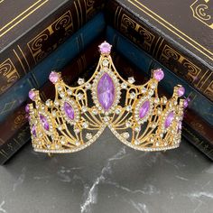 a gold tiara with pink stones sits on top of a pile of books in front of a bookcase