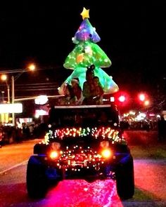 a jeep driving down a street with a christmas tree on top