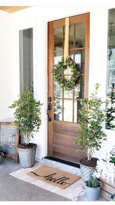 two potted plants sit on the front porch next to a door with a welcome mat