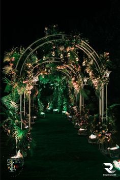 an outdoor wedding ceremony with lush greenery and flowers on the arch, lit up at night