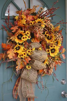 a wreath with sunflowers and fall leaves hanging on a blue front door,