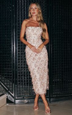 a woman standing in front of a metal gate wearing a dress with feathers on it