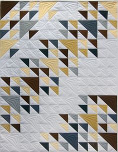 a white quilt with yellow, blue and brown triangles on it's sides is shown