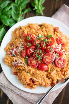 pasta with tomatoes and parmesan cheese on a plate next to a fork, napkin and basil leaves