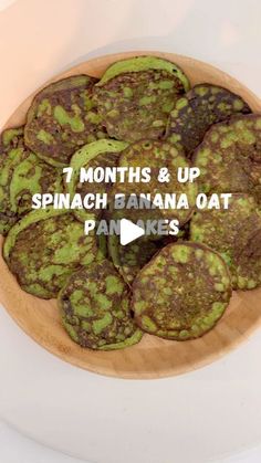 a wooden bowl filled with green pancakes on top of a white table