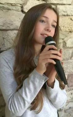 a young woman holding a microphone in front of a brick wall and looking up at the sky