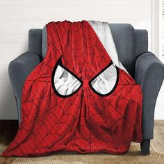 a spider - man blanket sitting on top of a couch next to a gray chair