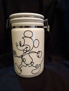 a white glass jar with a mickey mouse design on the front and bottom, sitting on a black surface