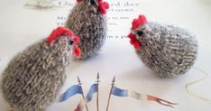 three knitted chickens sitting next to each other on a piece of paper with thread