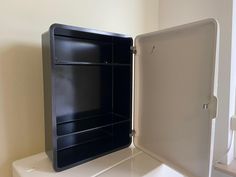 an open black refrigerator sitting on top of a white counter next to a window in a room